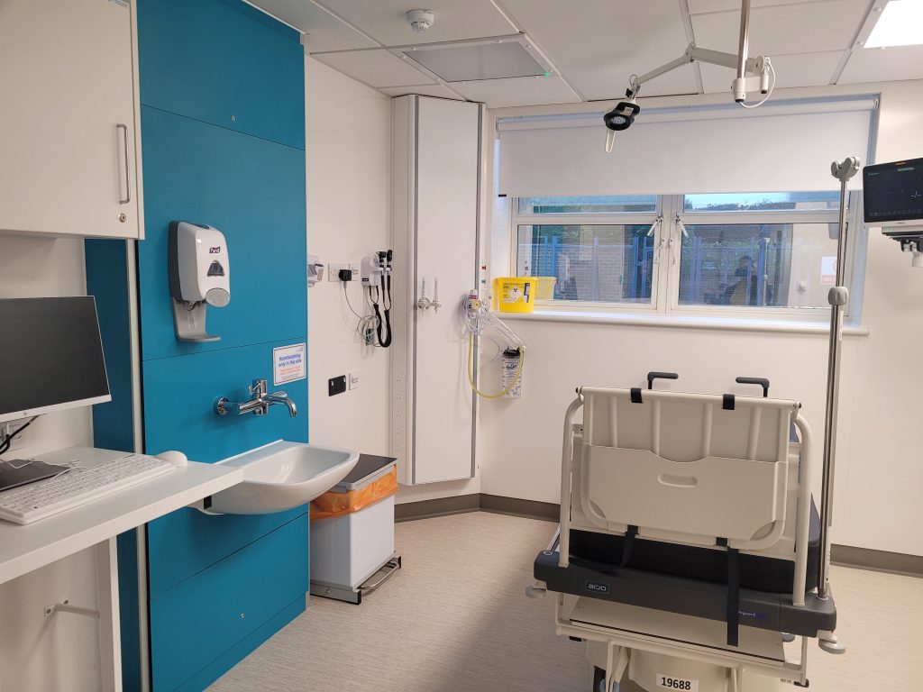 New ED cubicle with bed and other medical equipment. The walls feature a bright blue colour.